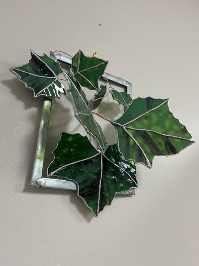 A square metal frame with large, dark green iridescent stained-glass sycamore leaves and copper wire veins fanning outward from a central branch.